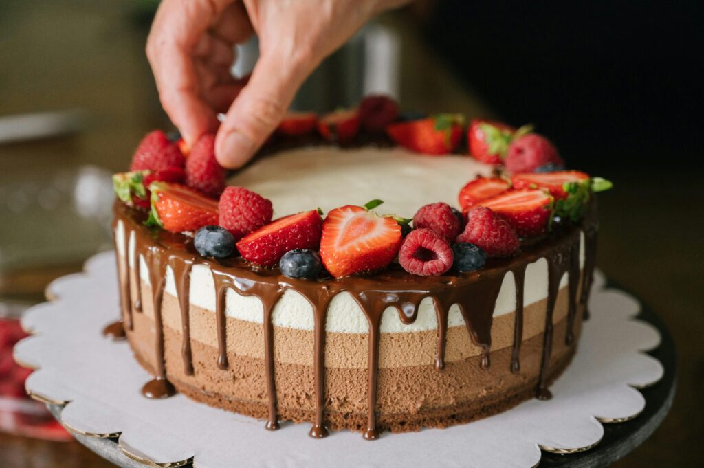 pexels-photo-18613264-18613264 Hand decorating a chocolate layer cake with fresh berries and cream frosting.